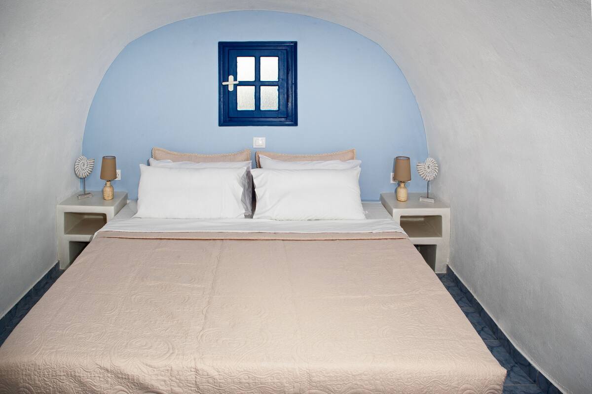 A bedroom with a large bed, two bedside tables, and a small window.