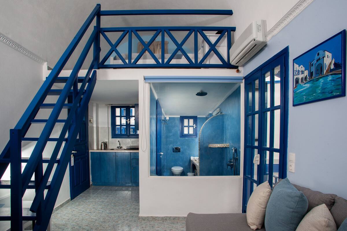 A room with a blue staircase, a kitchen, and a bathroom with a blue door.