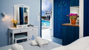 Une chambre d’hôtel avec un lit, une coiffeuse avec un miroir, un lavabo et une vue sur une piscine et les bâtiments environnants.