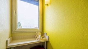 A small room with a window, a red stool, a shelf with a kettle, cups, and a tray, and a yellow textured wall. - Comfort Hotel Orleans Olivet (Olivet)