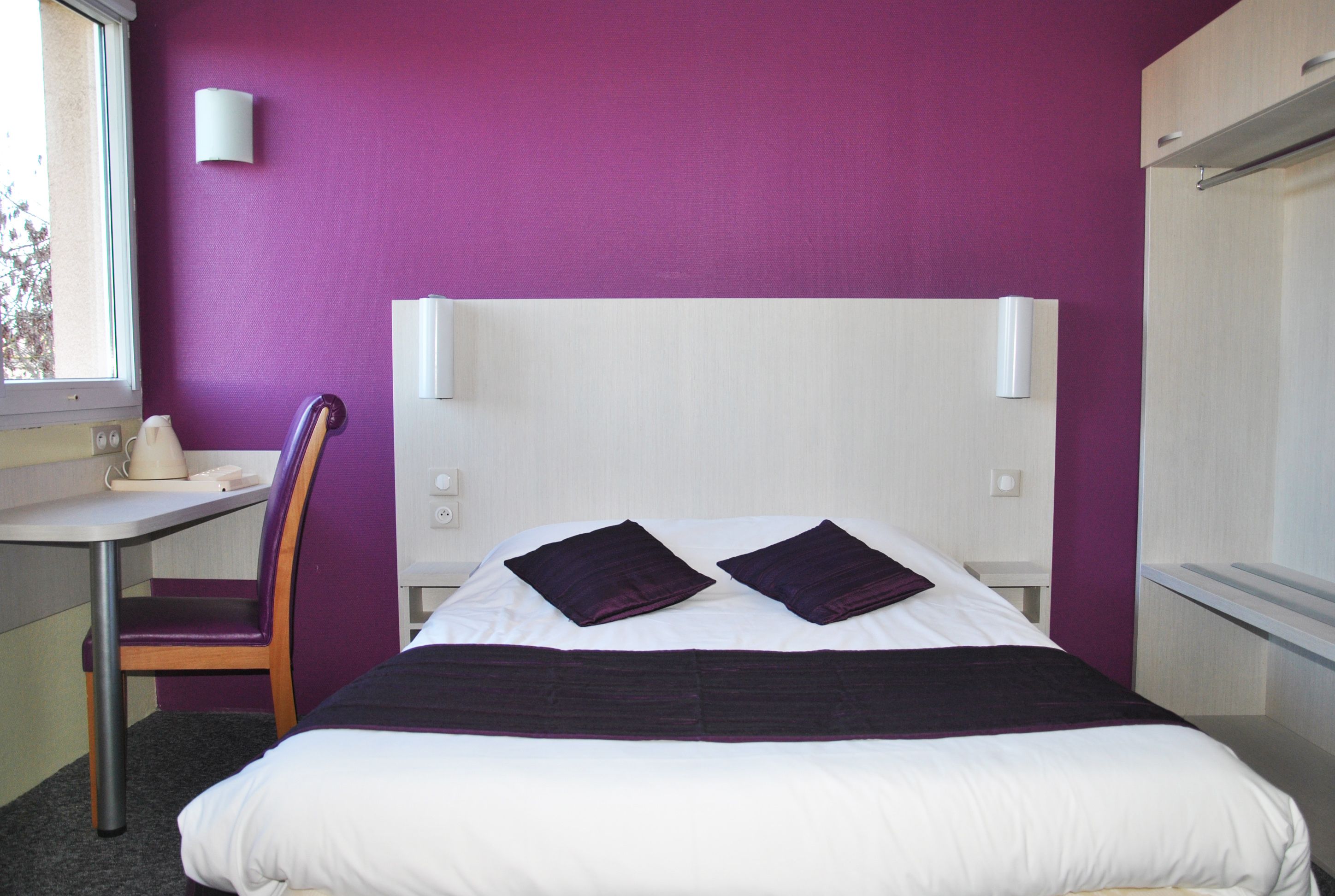 A hotel room with a bed, a desk, and a chair.