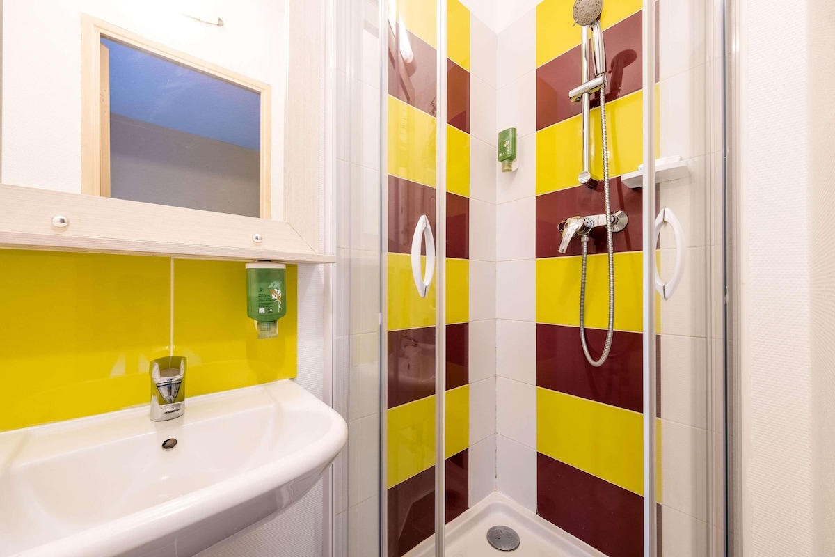 A bathroom with a white sink, a shower with a glass door, and yellow and red tiles.