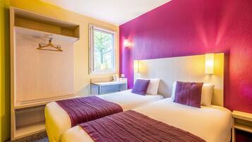 Habitación de hotel con dos camas, un armario, un escritorio pequeño y una ventana.