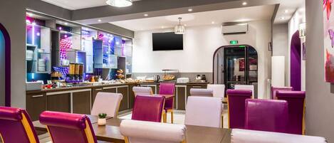 A modern restaurant with purple and white chairs, a bar area with glass shelves, and a flat-screen TV mounted on the wall.