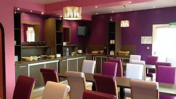 A modern restaurant with purple and beige chairs, a counter with various items, and a television on the wall.
