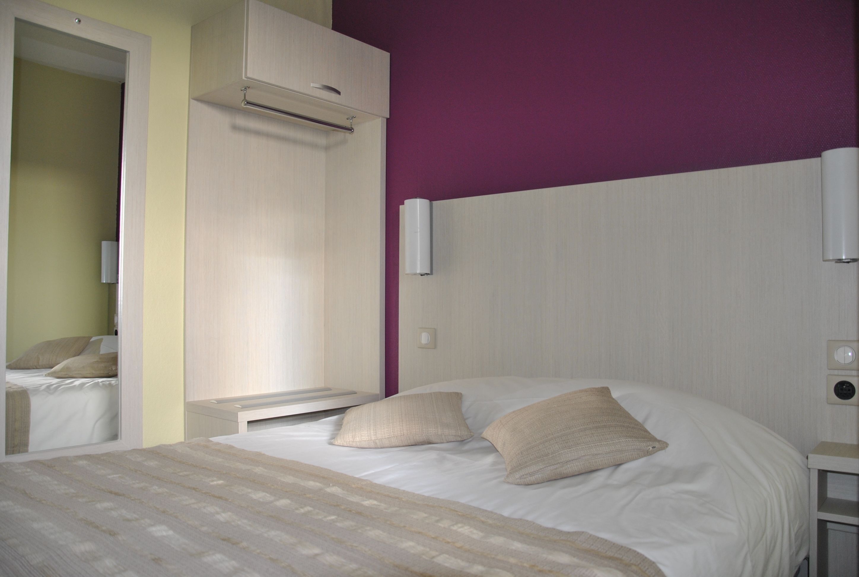 A neatly made bed with two pillows, a bedside table, a nightstand, and a wall-mounted air conditioner.