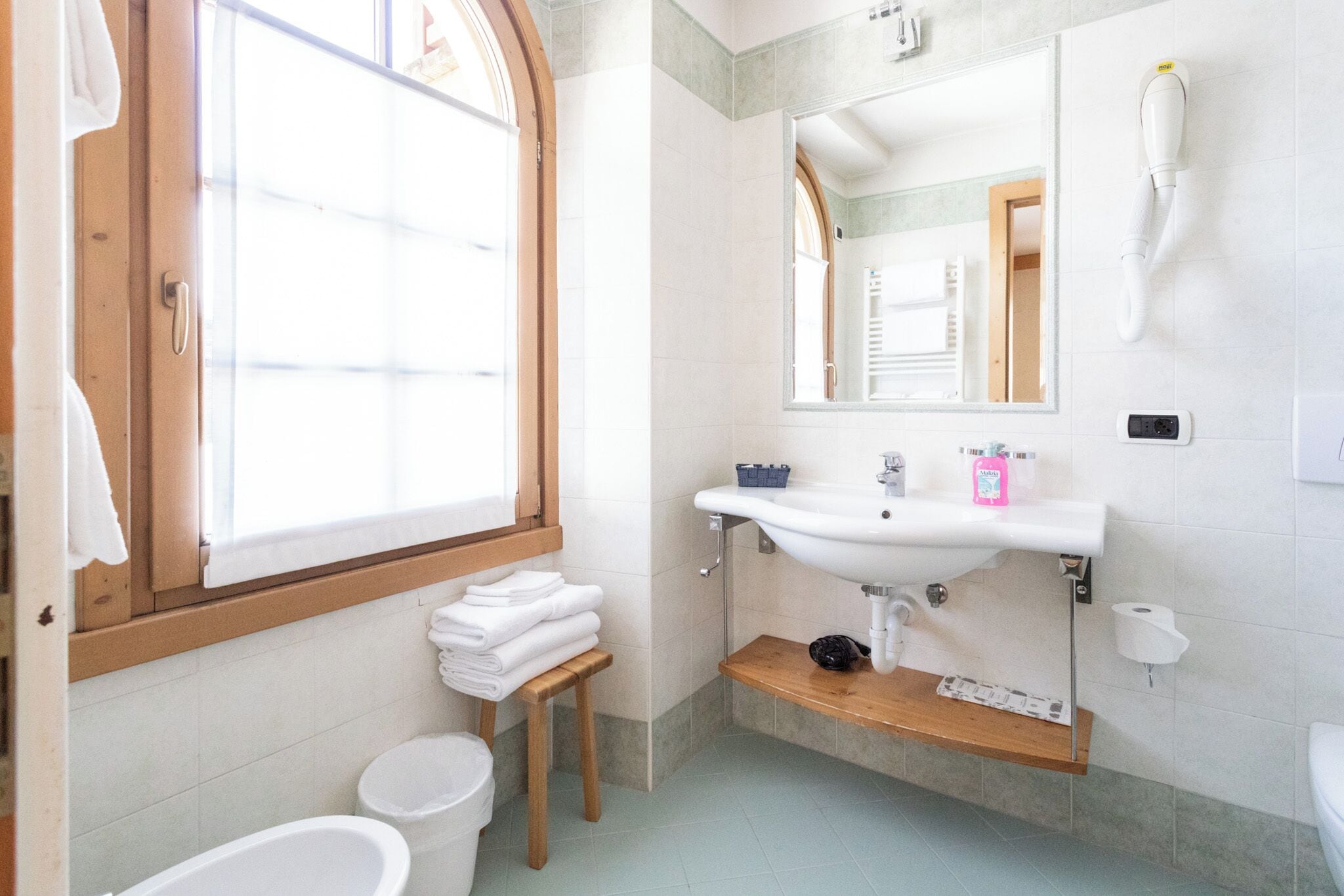 A bathroom with a window, a sink, a mirror, and a toilet.