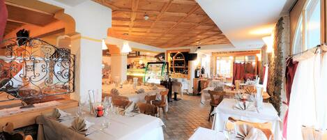 Interior de restaurant amb bigues de sostre de fusta, tovallons blancs i taules ben ordenades.