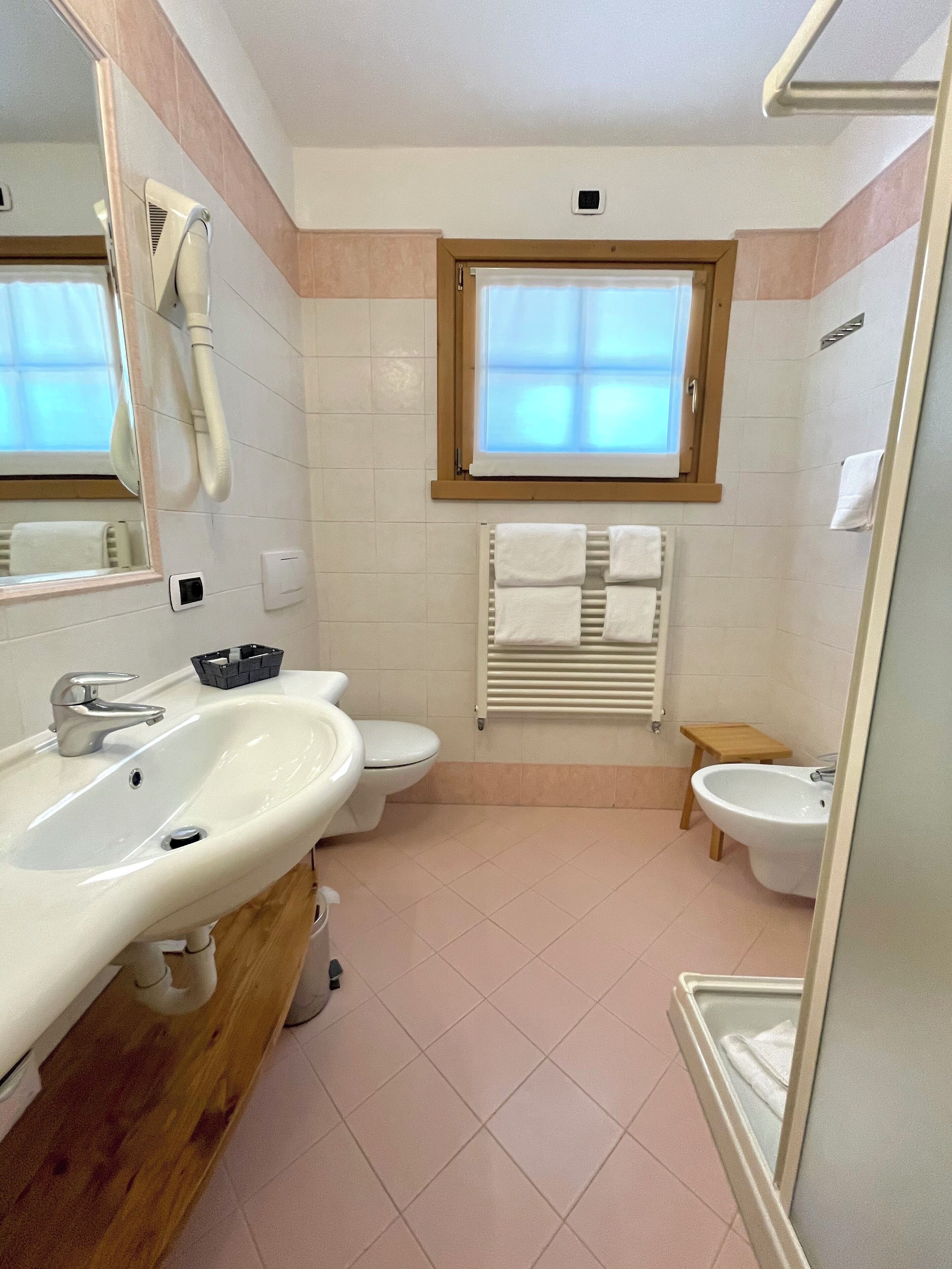 A modern bathroom with a sink, toilet, bidet, and a window.