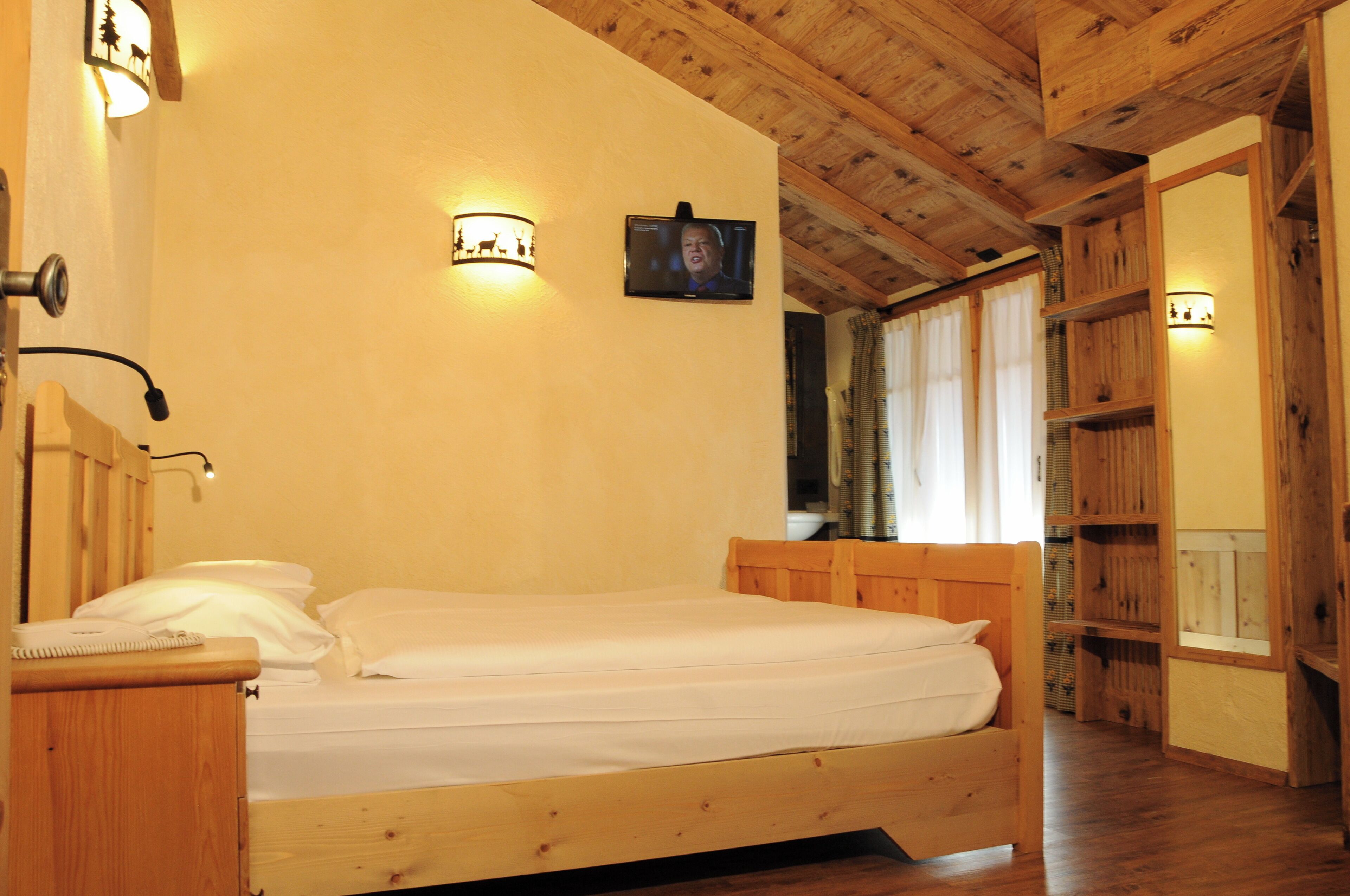 Un lit en bois dans une pièce où est fixée une télévision au mur, ainsi qu’une armoire en bois.