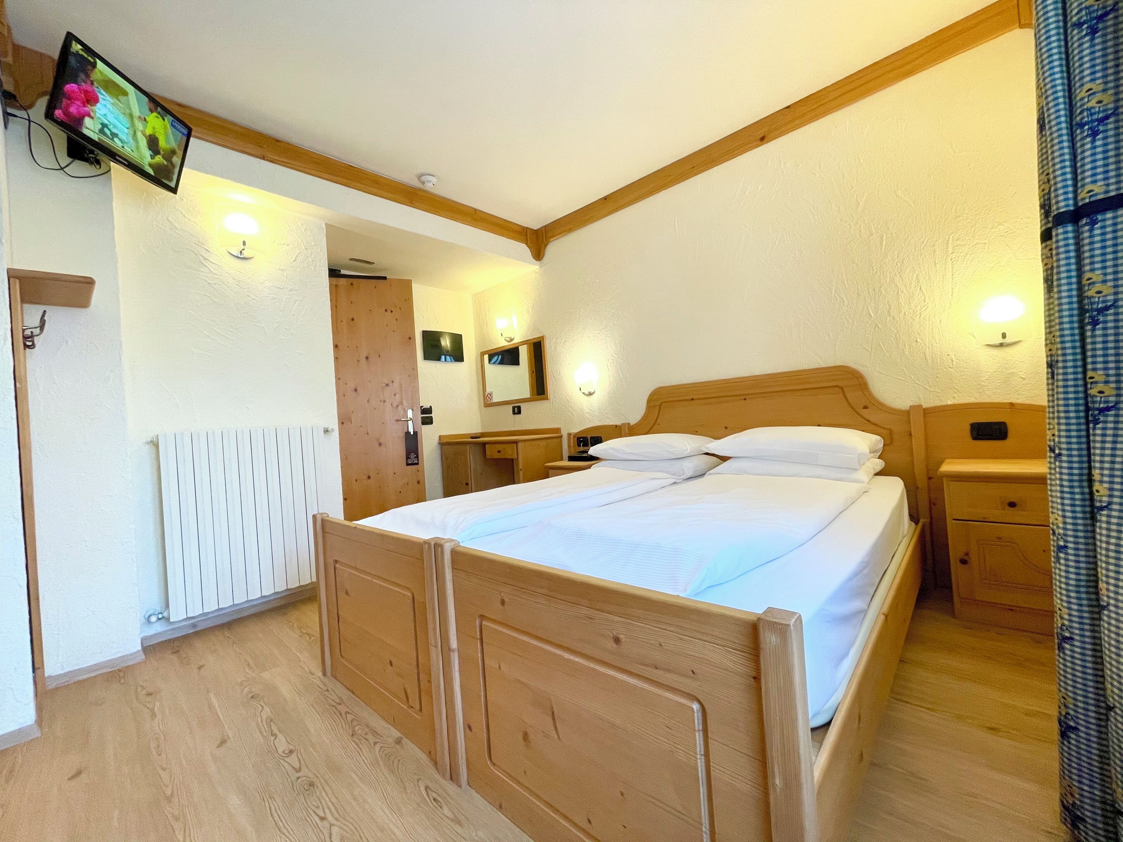Una camera da letto con un letto di legno, comodini, una TV montata a parete e un termosifone.