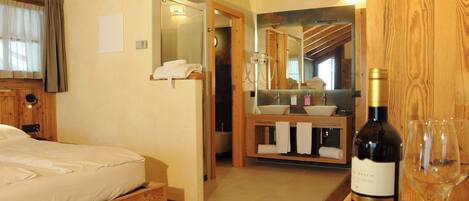 A wooden-framed bedroom with a bed, a bathroom with a sink and mirror, and a bottle of wine on a table.