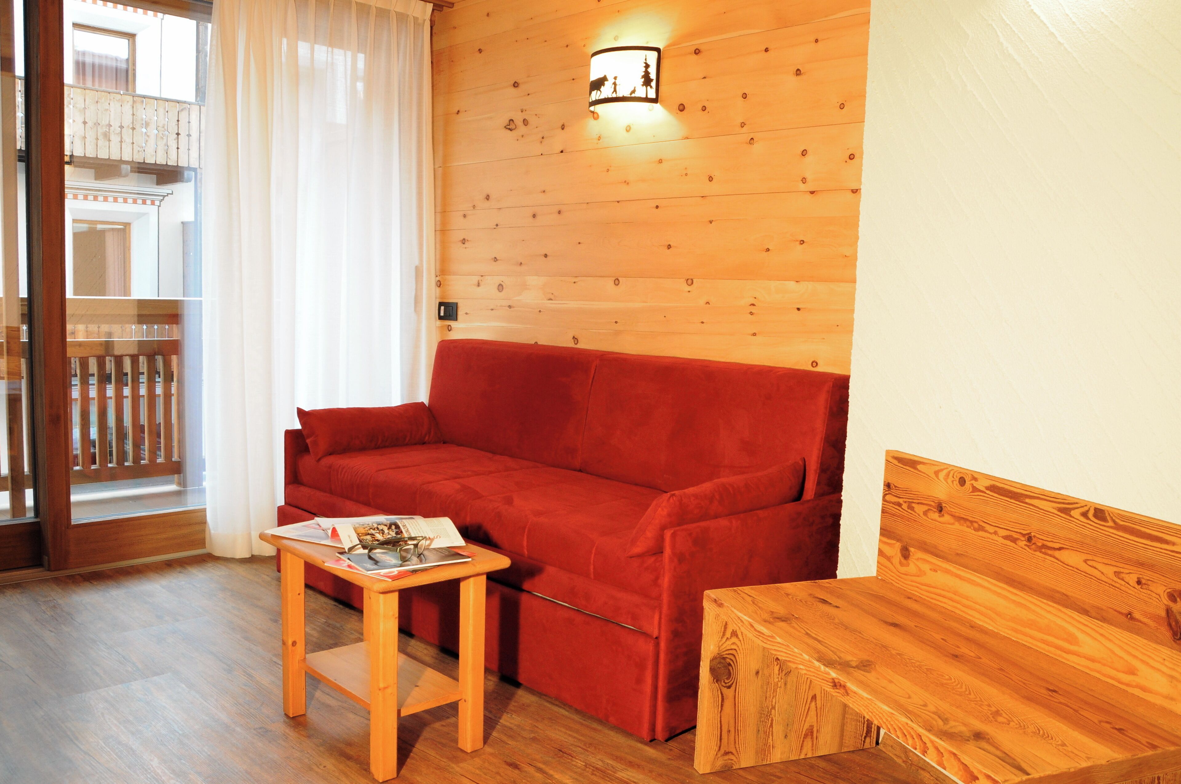 A wooden-floored living area with a red sofa, a small wooden table, and a wooden bench.