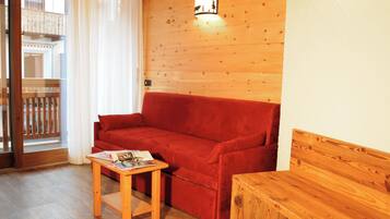 A wooden-floored living area with a red sofa, a small wooden table, and a wooden bench.