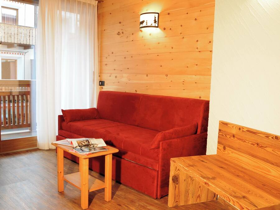 A wooden-floored living area with a red sofa, a small wooden table, and a wooden bench.