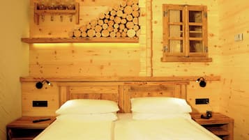 Habitación de cabaña de madera con una cama, mesitas de noche, estante con frascos, una ventana y un aplique de pared.