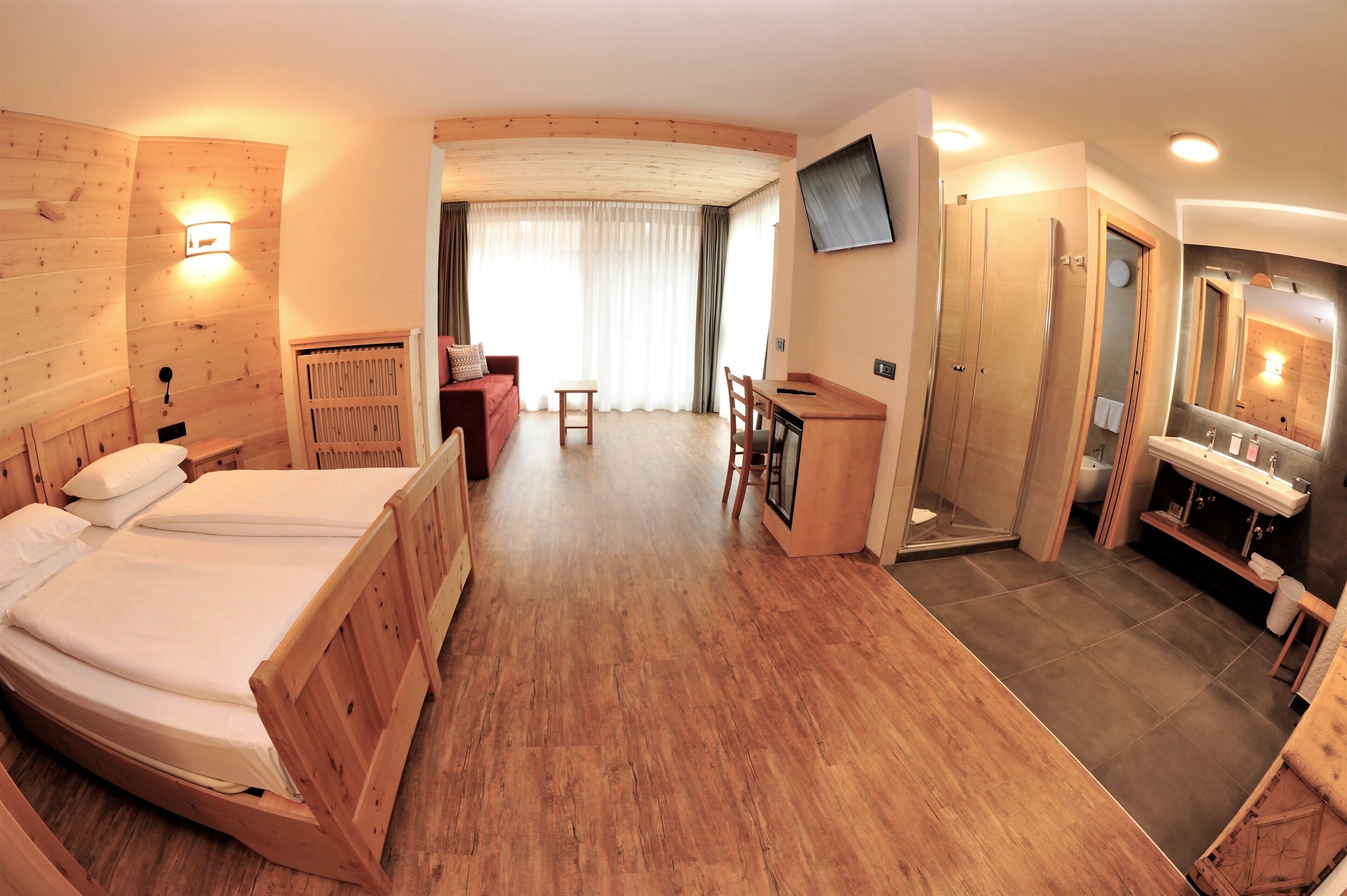 A room with a bed, desk, chair, and a bathroom with a mirror and sink.