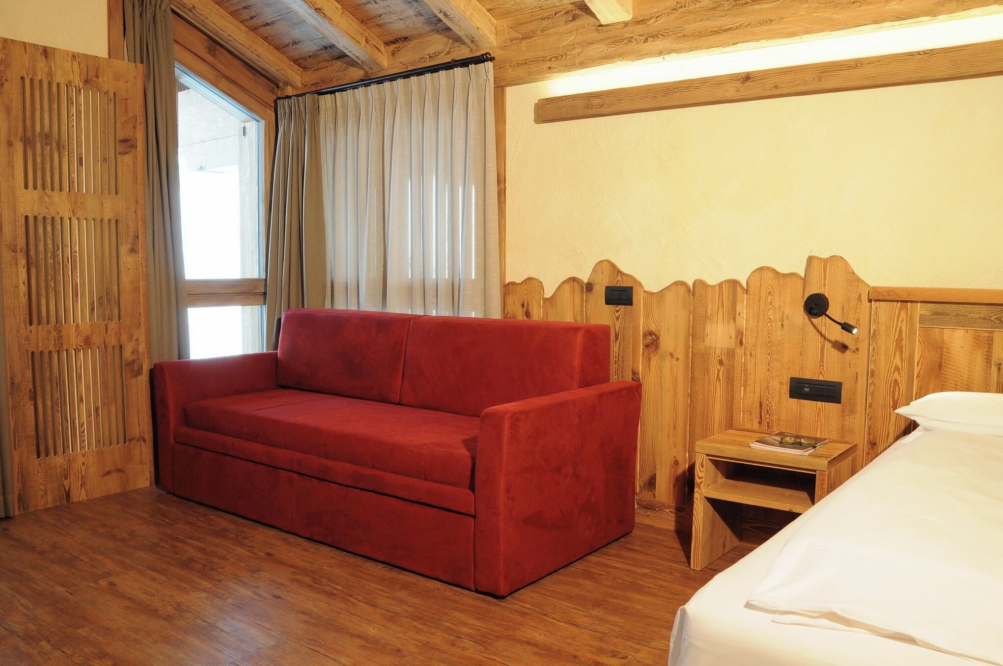 A wooden room with a red sofa, a wooden nightstand, and a bed.