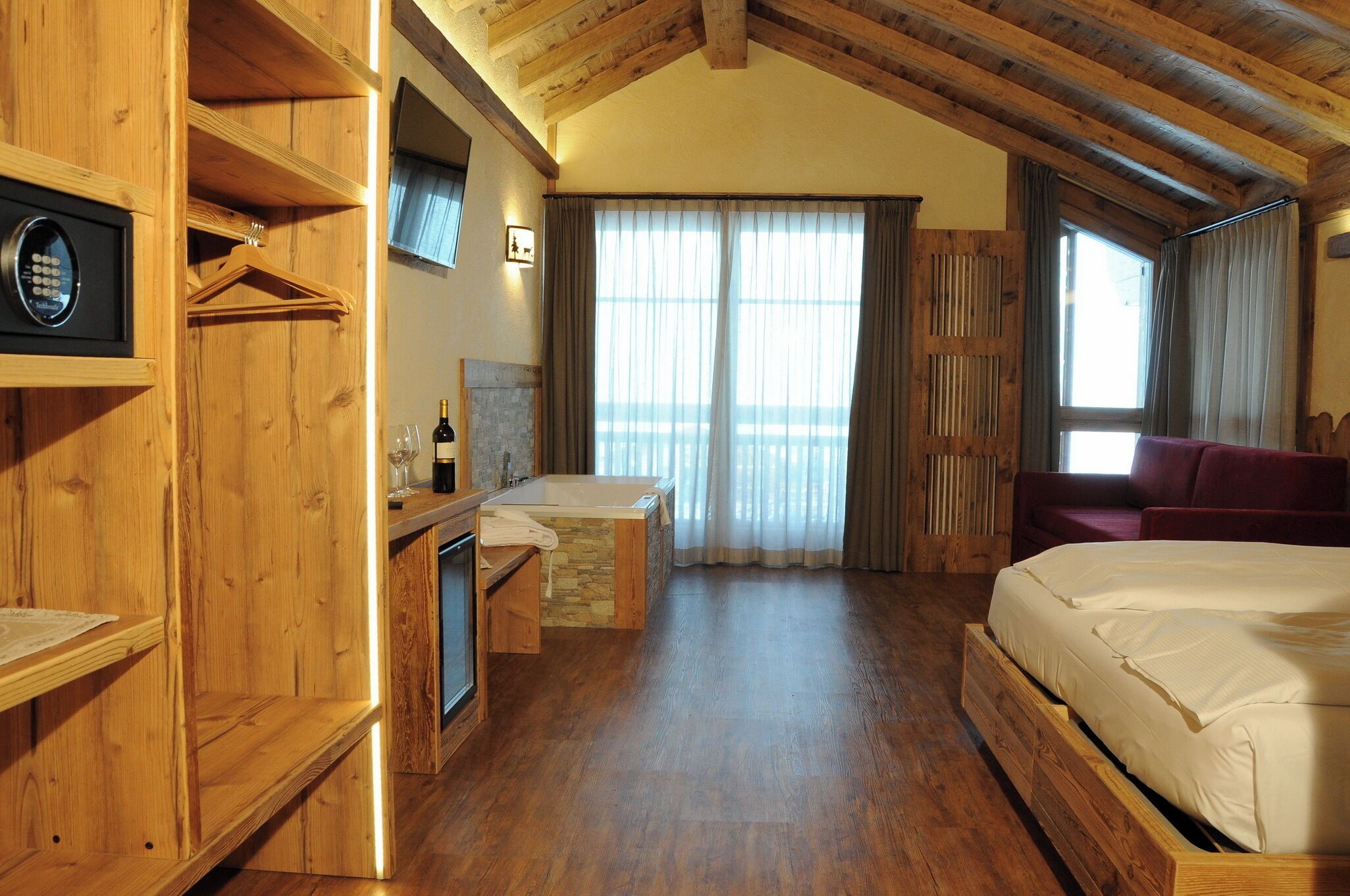 Un dormitorio con piso de madera, una cama, una mesita con una botella y un televisor montado en la pared.