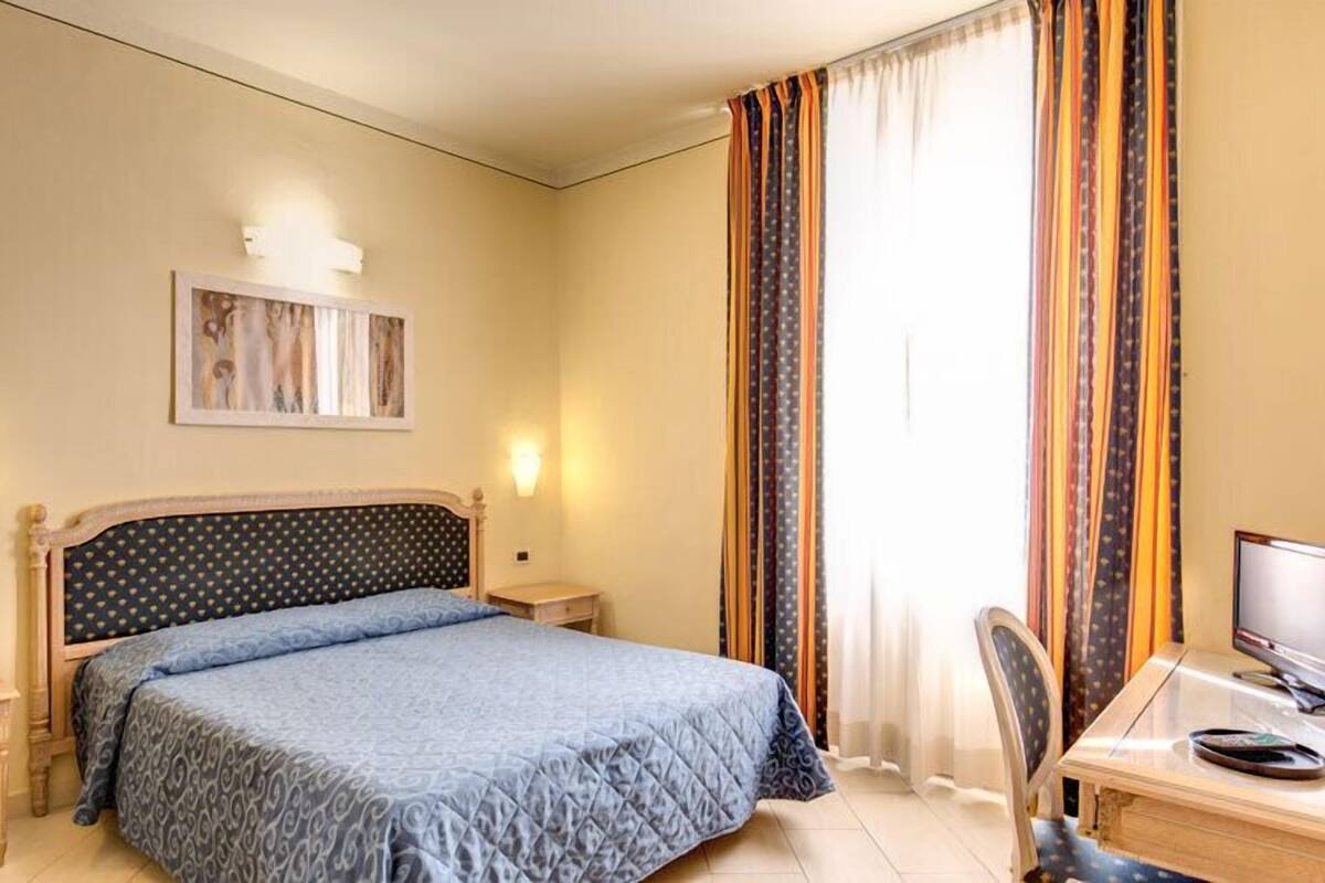 A hotel room with a bed, a desk with a chair, a television, and curtains.