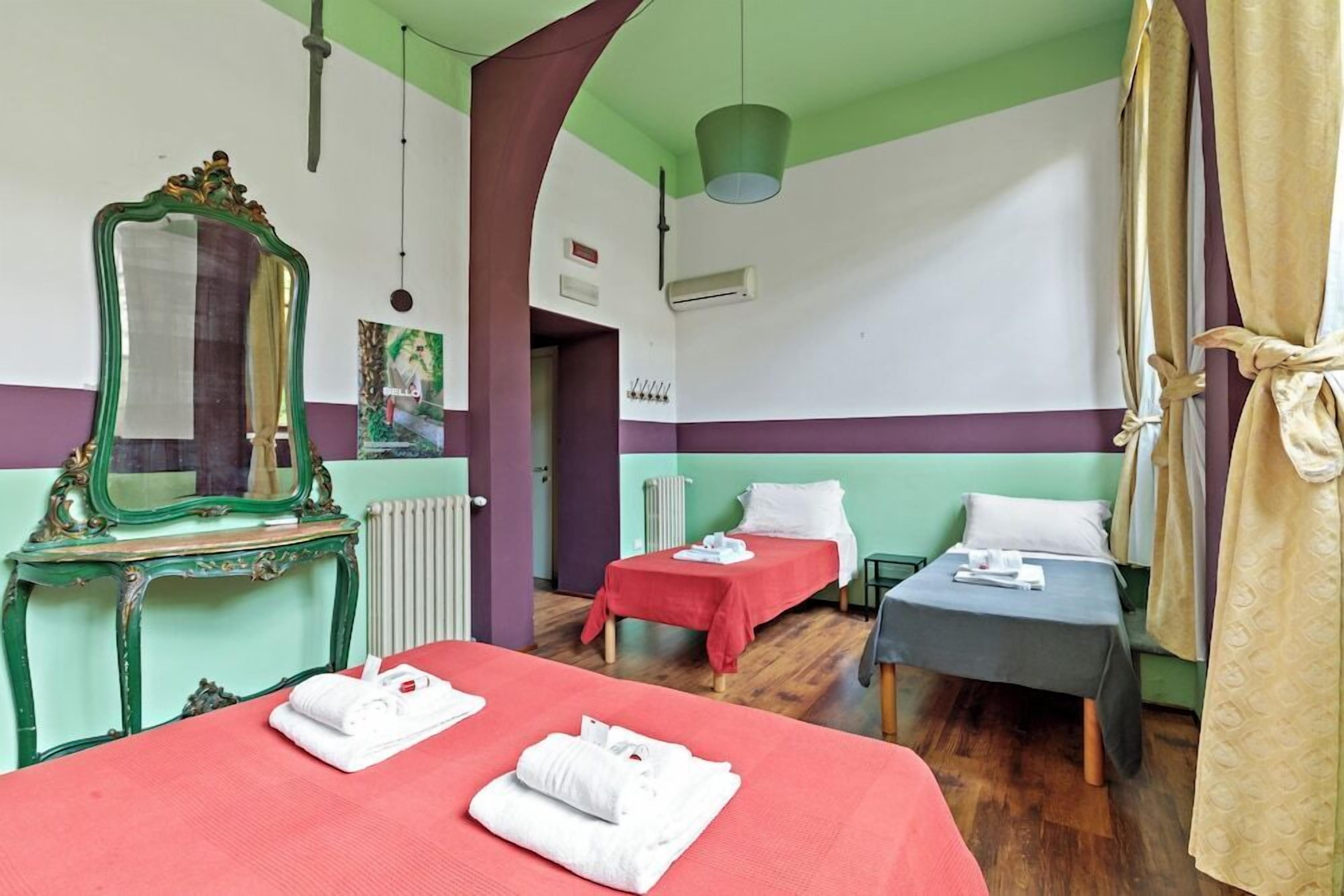 A hotel room with two beds, a mirror, a radiator, and a green ceiling.