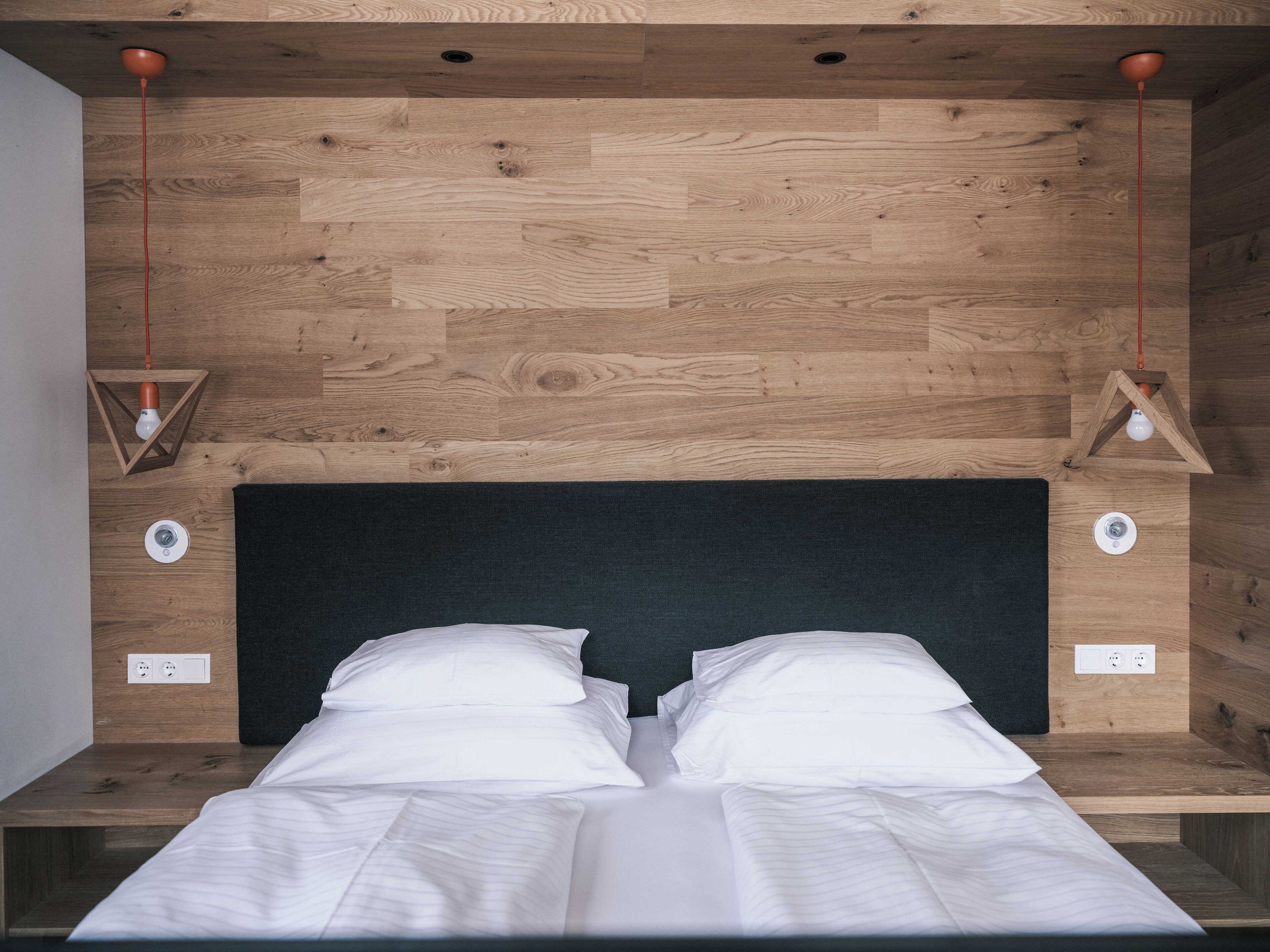 A bed with white linens in a room with wooden flooring and a dark headboard.