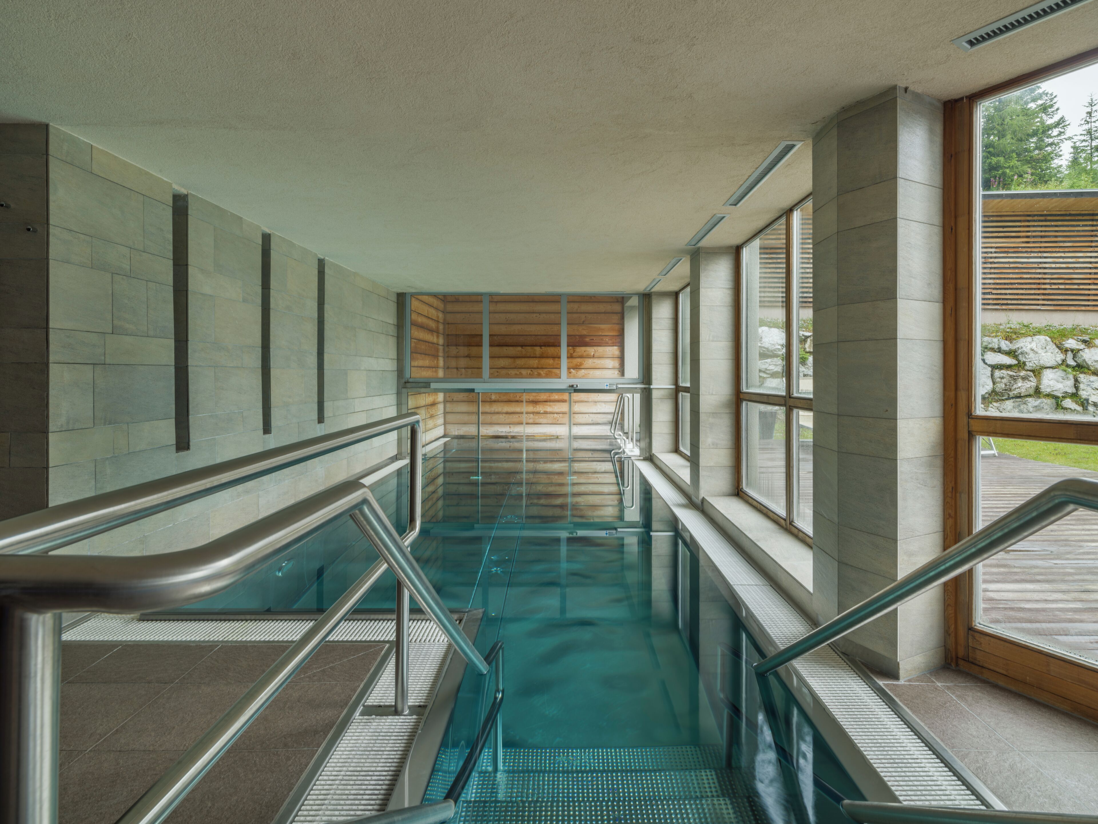 A modern indoor pool area with glass railings and a view of the outdoors.