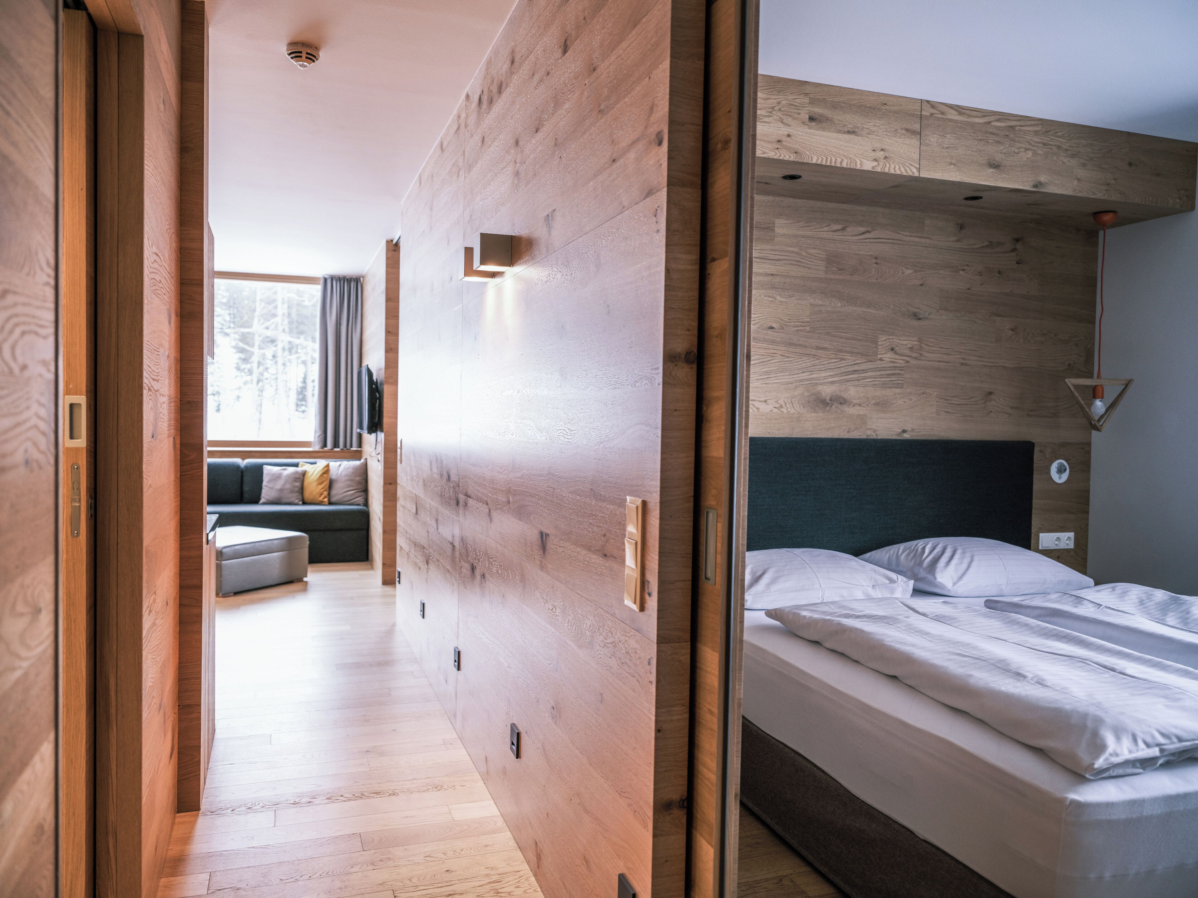 A modern bedroom with a wooden headboard, a bed with white linens, and a wooden floor.