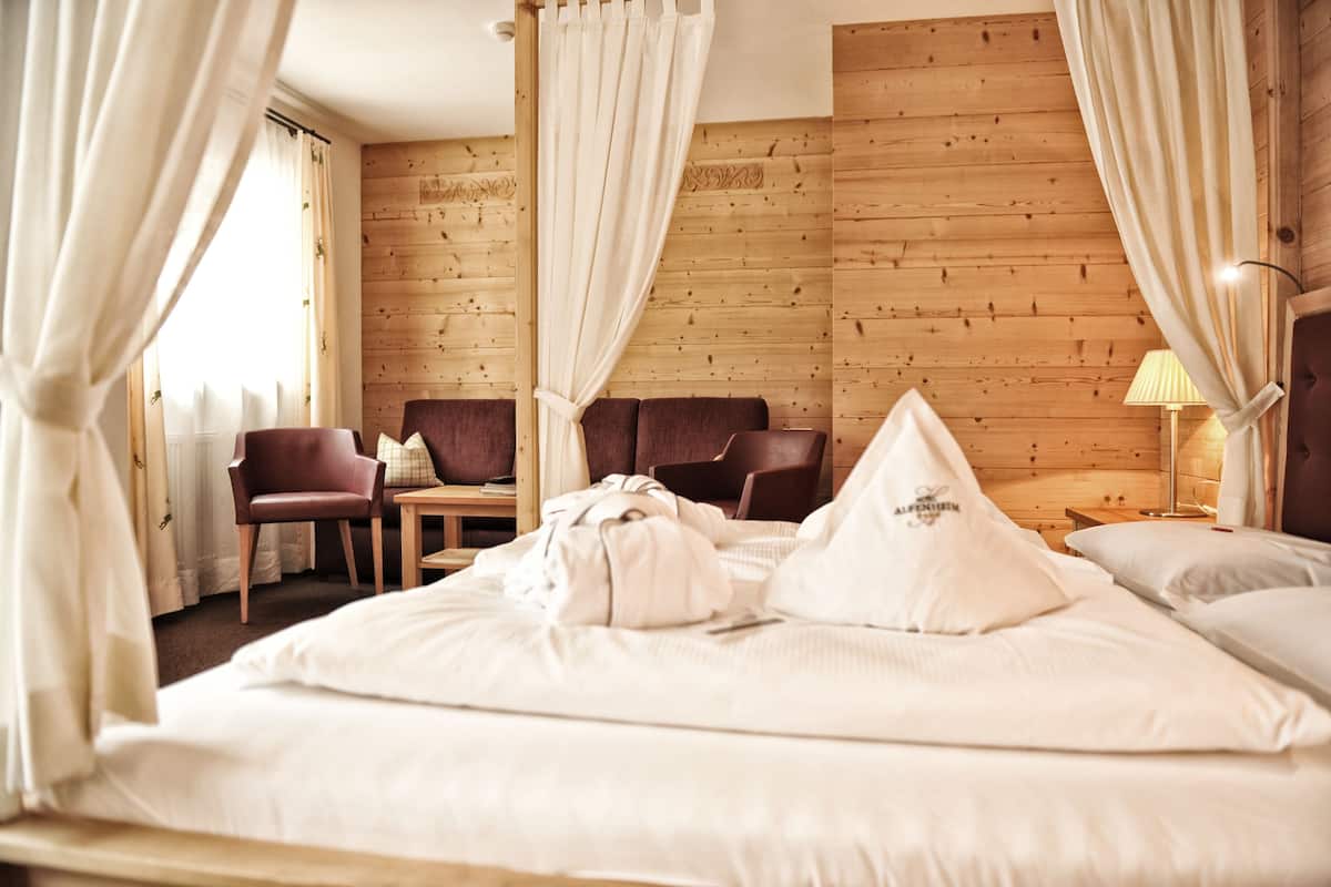Habitación de hotel con pared de madera, cama con sábanas blancas, dos sillas, una mesa y una lámpara.