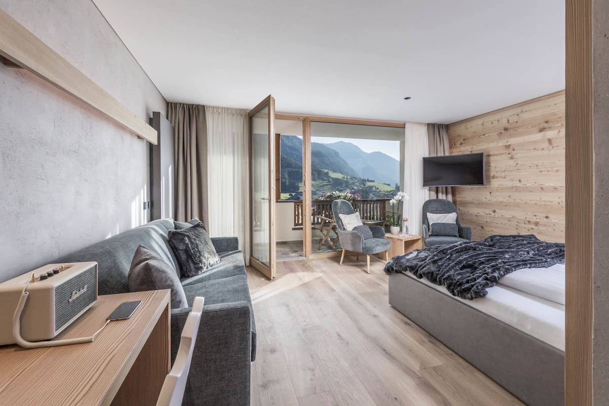 Una habitación de hotel moderna con sofá, cama, televisor y balcón con vistas a la montaña.