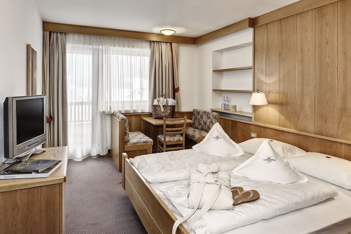 Una habitación de hotel con cama, escritorio, silla, televisor y lámpara.