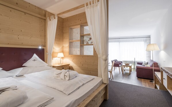 A well-lit room with a bed, a nightstand, a lamp, a sofa, and a dining table. - Alpenheim Charming & Spa Hotel (Ortisei)