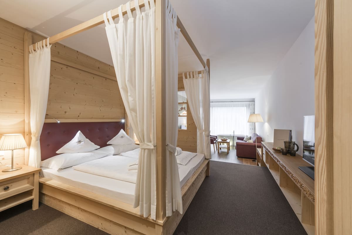 Una cama con dosel y cortinas blancas, un cabecero de madera y una mesita de noche con una lámpara.
