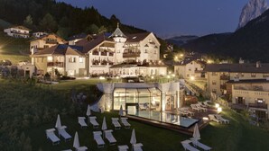 Una piscina con copertura in vetro, diverse poltrone relax e uno sfondo montuoso.