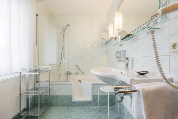 A modern bathroom with a glass shower enclosure, a white sink, and a glass shelf with toiletries. - Hotel Schönegg (Seefeld in Tirol)
