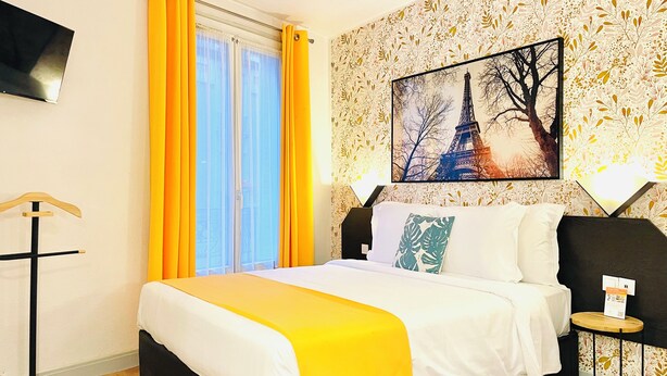 A hotel room with a bed, a window with yellow curtains, a wall-mounted TV, and a painting of the Eiffel Tower. - Appart Hôtel Boulogne Résidence (Boulogne-Billancourt)
