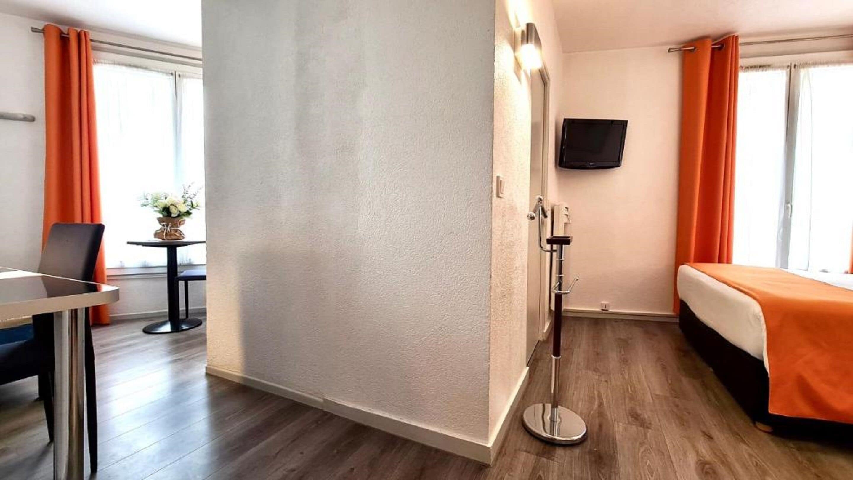 A hotel room with a bed, a desk, a chair, a TV mounted on the wall, and a shower area.