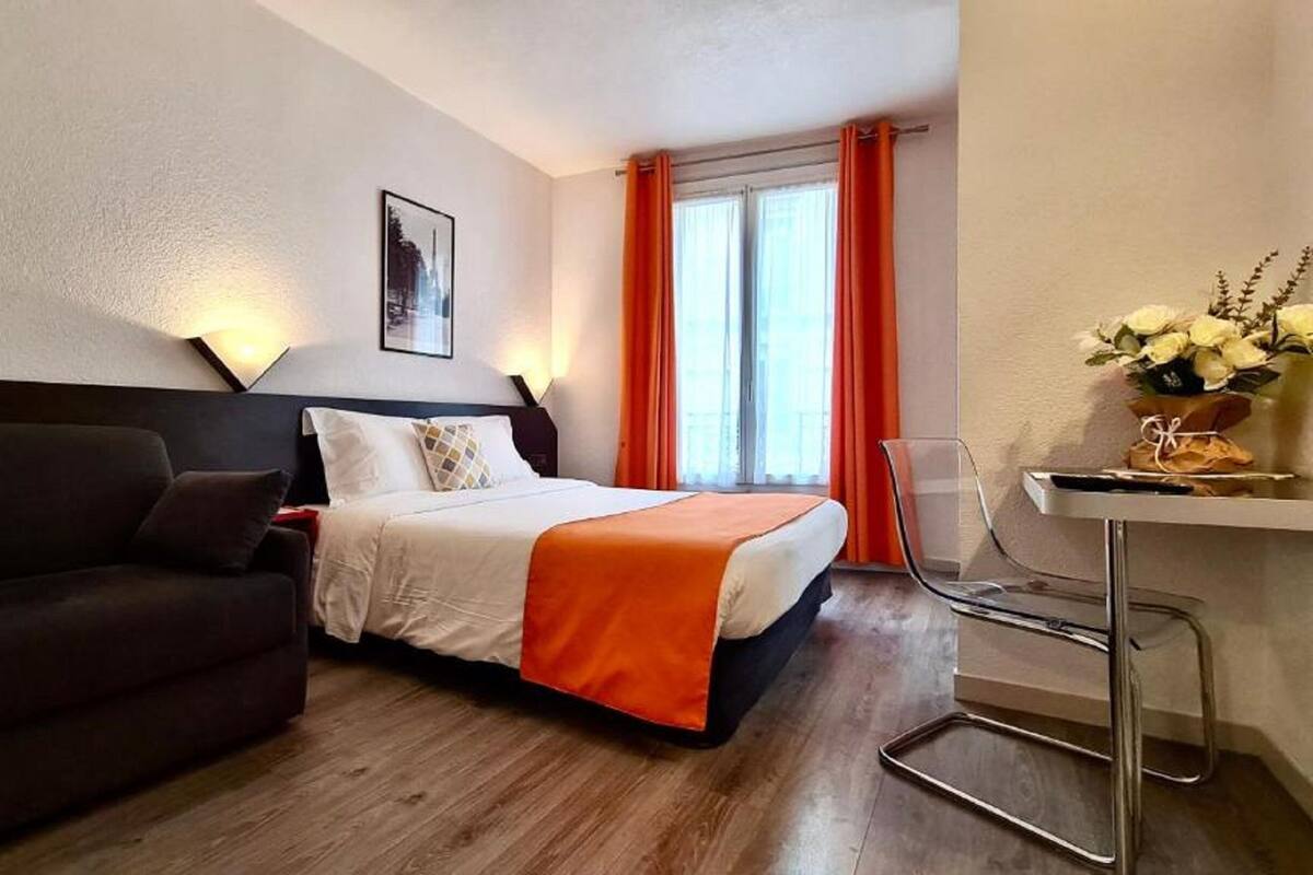 A hotel room with a bed, a sofa, a desk with a chair, and a window with curtains.