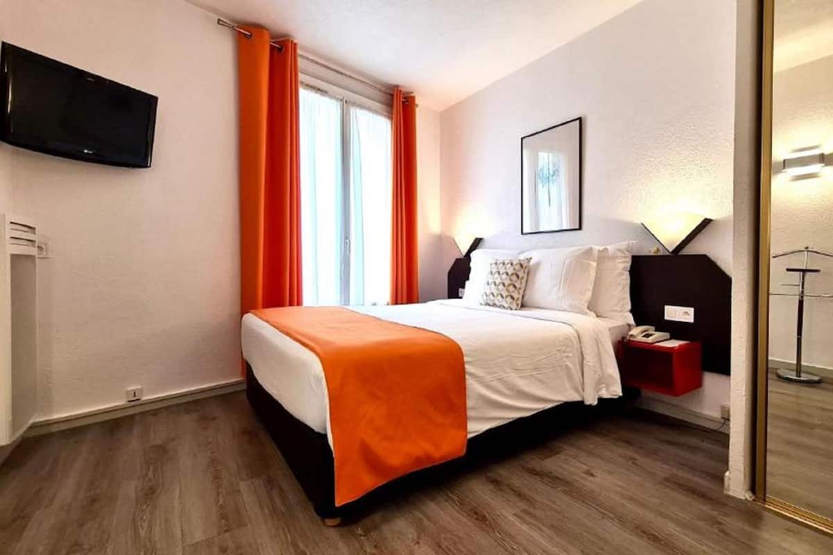 A hotel room with a bed, a bedside table with a phone, a mirror, and a TV mounted on the wall.