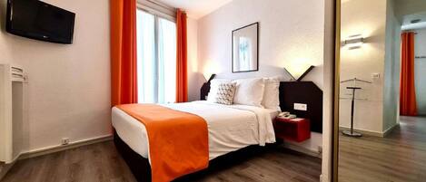A hotel room with a bed, a bedside table with a phone, a mirror, and a TV mounted on the wall.