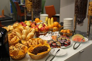 A buffet with various food items including fruits, pastries, and condiments.