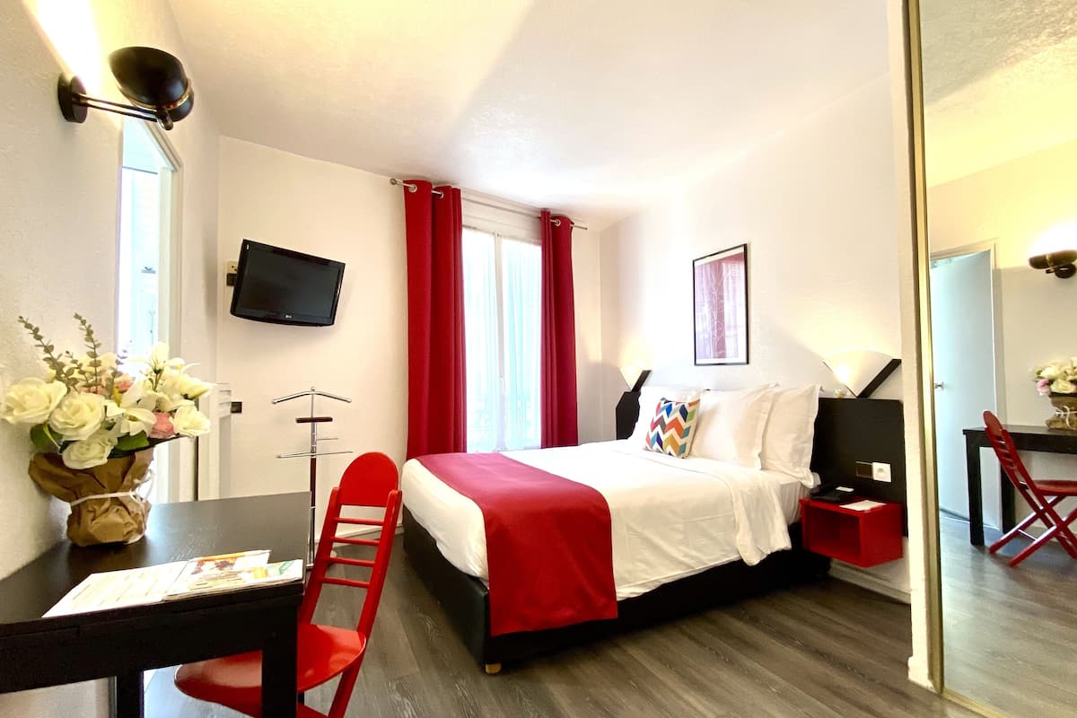 A hotel room with a bed, a desk, a chair, a TV, and a mirror.