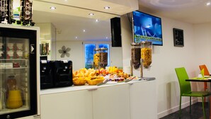 A breakfast bar with various food items and a television screen displaying a news program. - Appart Hôtel Boulogne Résidence (Boulogne-Billancourt)