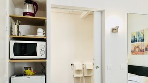A compact hotel room with a kitchenette, a microwave, a refrigerator, and a bed with white bedding. - Appart Hôtel Boulogne Résidence (Boulogne-Billancourt)