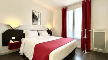 A hotel room with a bed, a nightstand with a phone, a wall-mounted picture, and a window with red curtains.