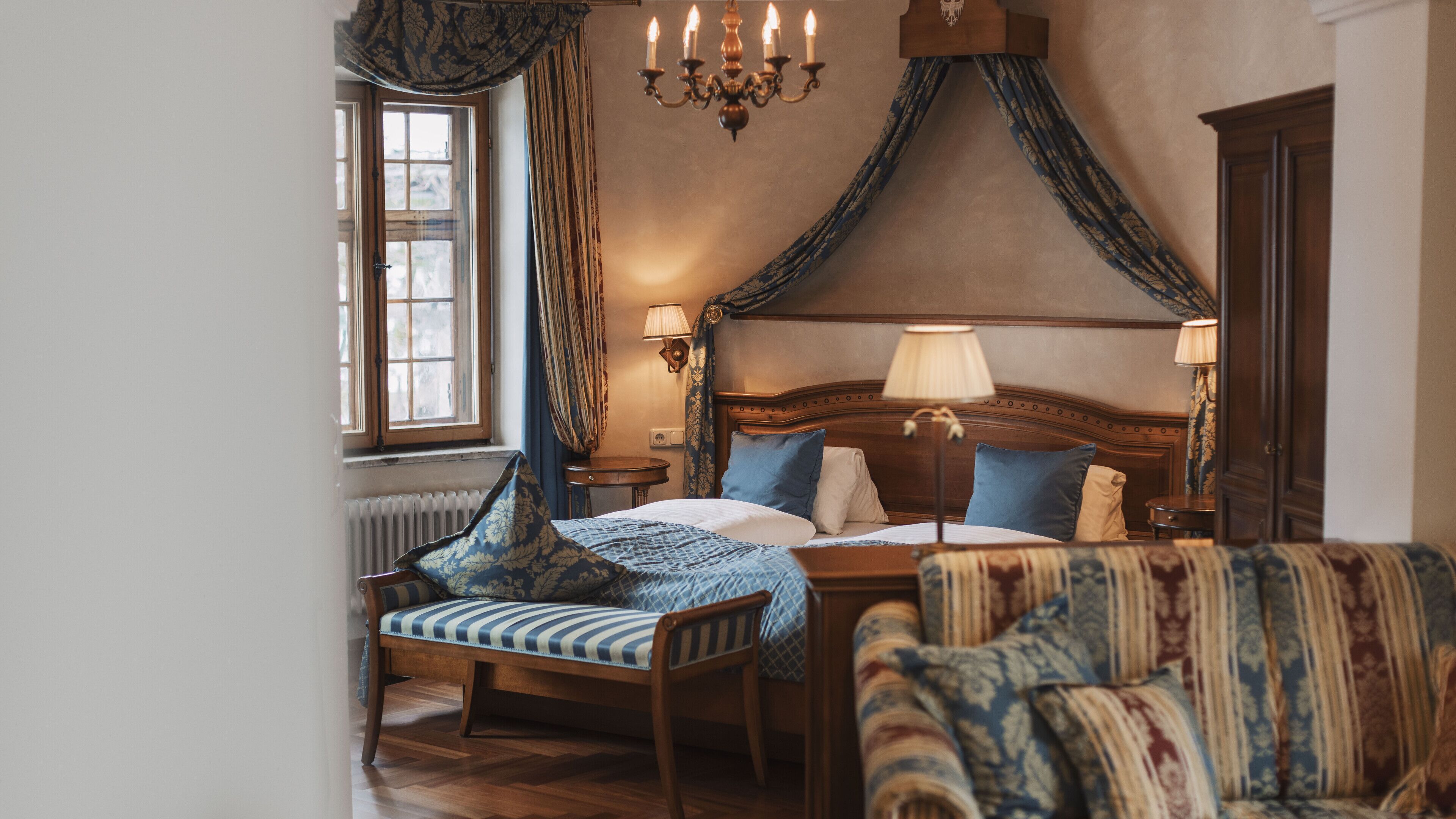 Ein traditionell eingerichtetes Schlafzimmer mit Himmelbett, Holzstuhl, einer Couch und einer Kandelaber.