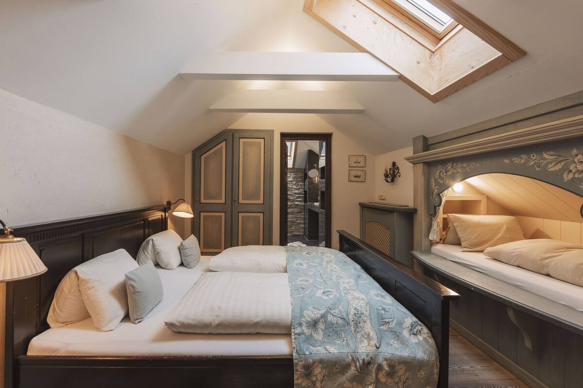 Un dormitorio con cama, mesitas de noche, lámpara, espejo y tragaluz.