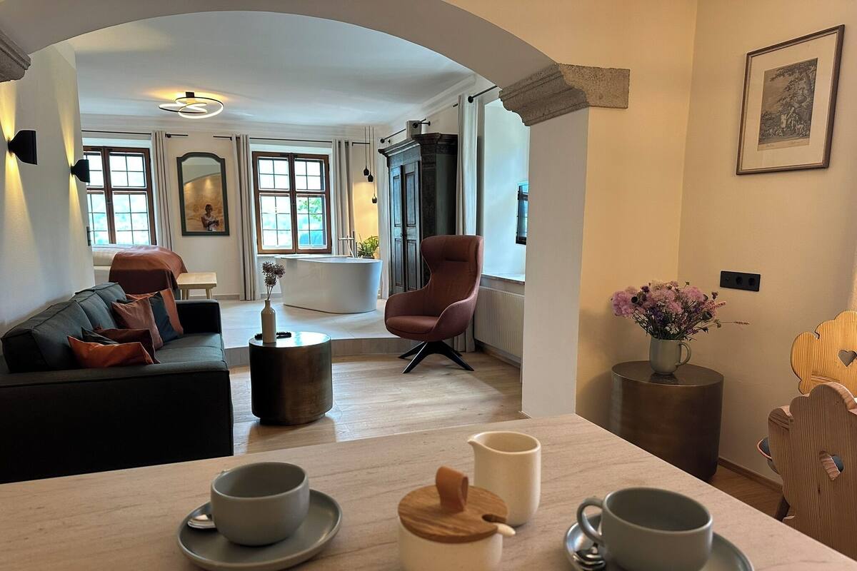 Una sala moderna con sofá, sillón, mesa de centro y vista a un baño con bañera.