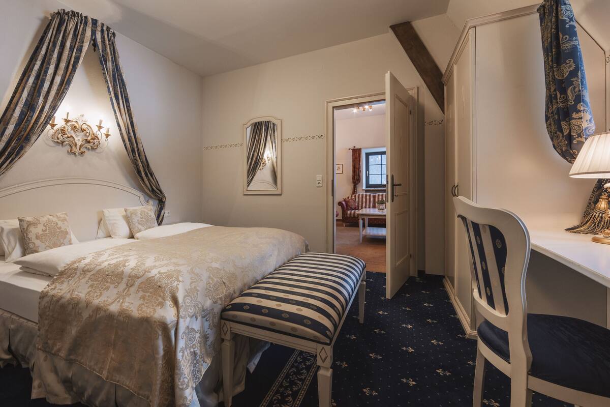 Un dormitorio con cama, mesita de noche, silla y vistas a otra habitación.