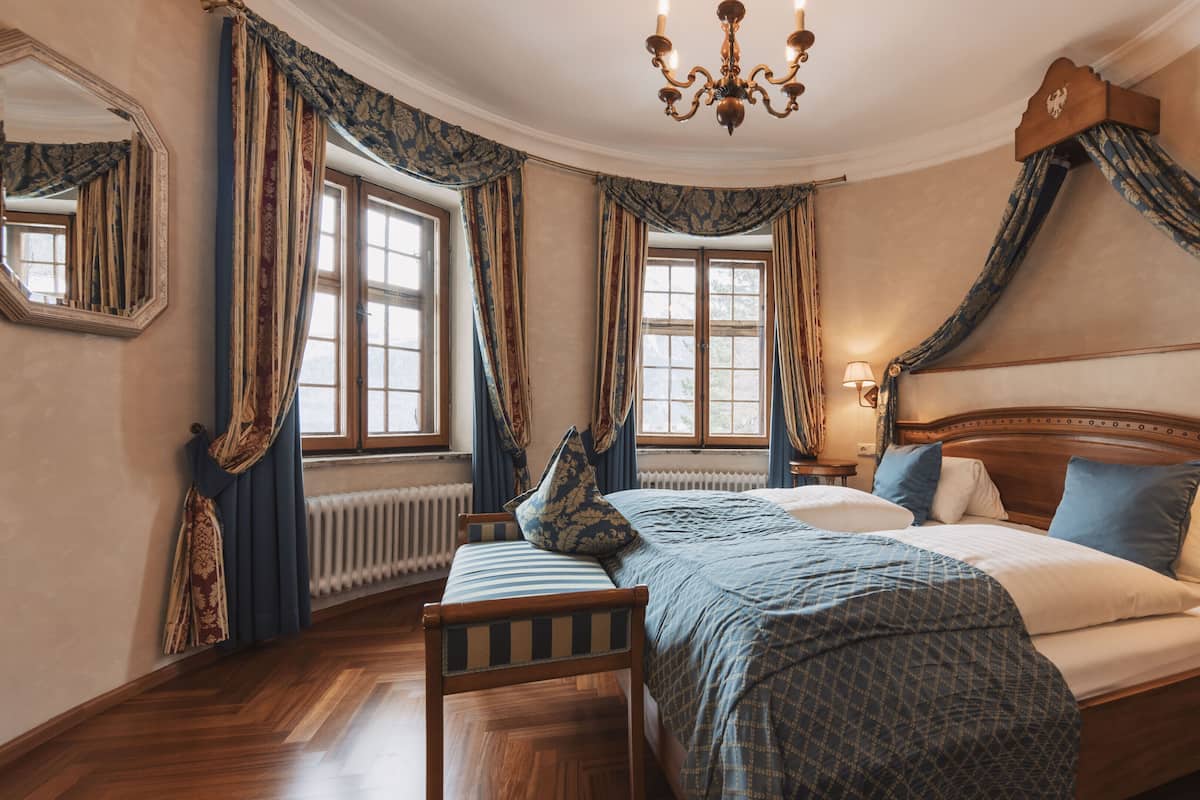 Un dormitorio tradicional con una cama grande, una silla de madera, una araña y decoración clásica.
